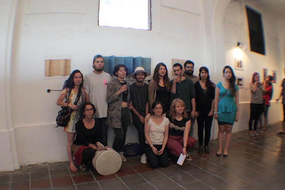 Doce personas, varias de pie y otras arrodilladas, posando para una fotografía delante de una pared blanca con una obra de arte, y una ventana blanca