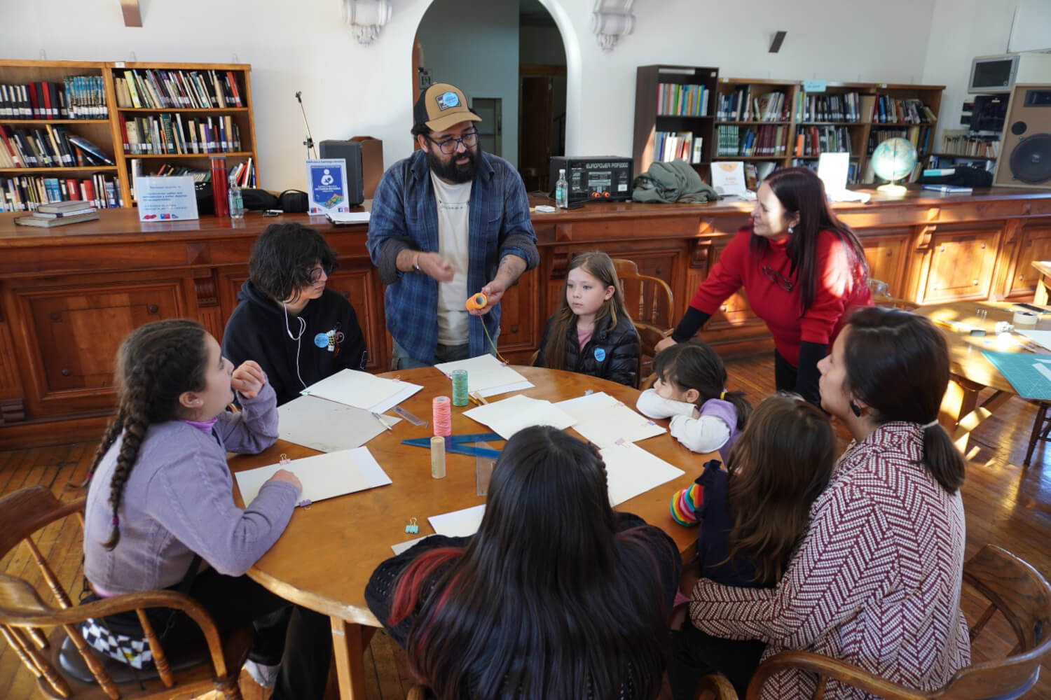 Grupo de niños y niñas en torno a una mesa redonda, participando en un taller de encuadernación